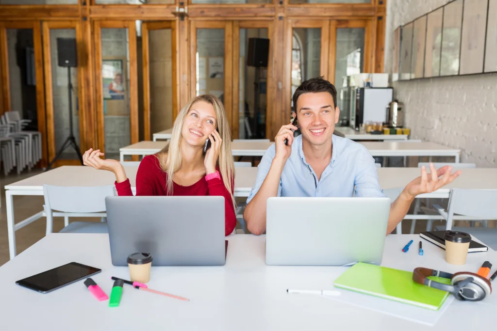 Jovens sorridentes trabalhando em laptops e atendendo chamadas em um ambiente de trabalho colaborativo